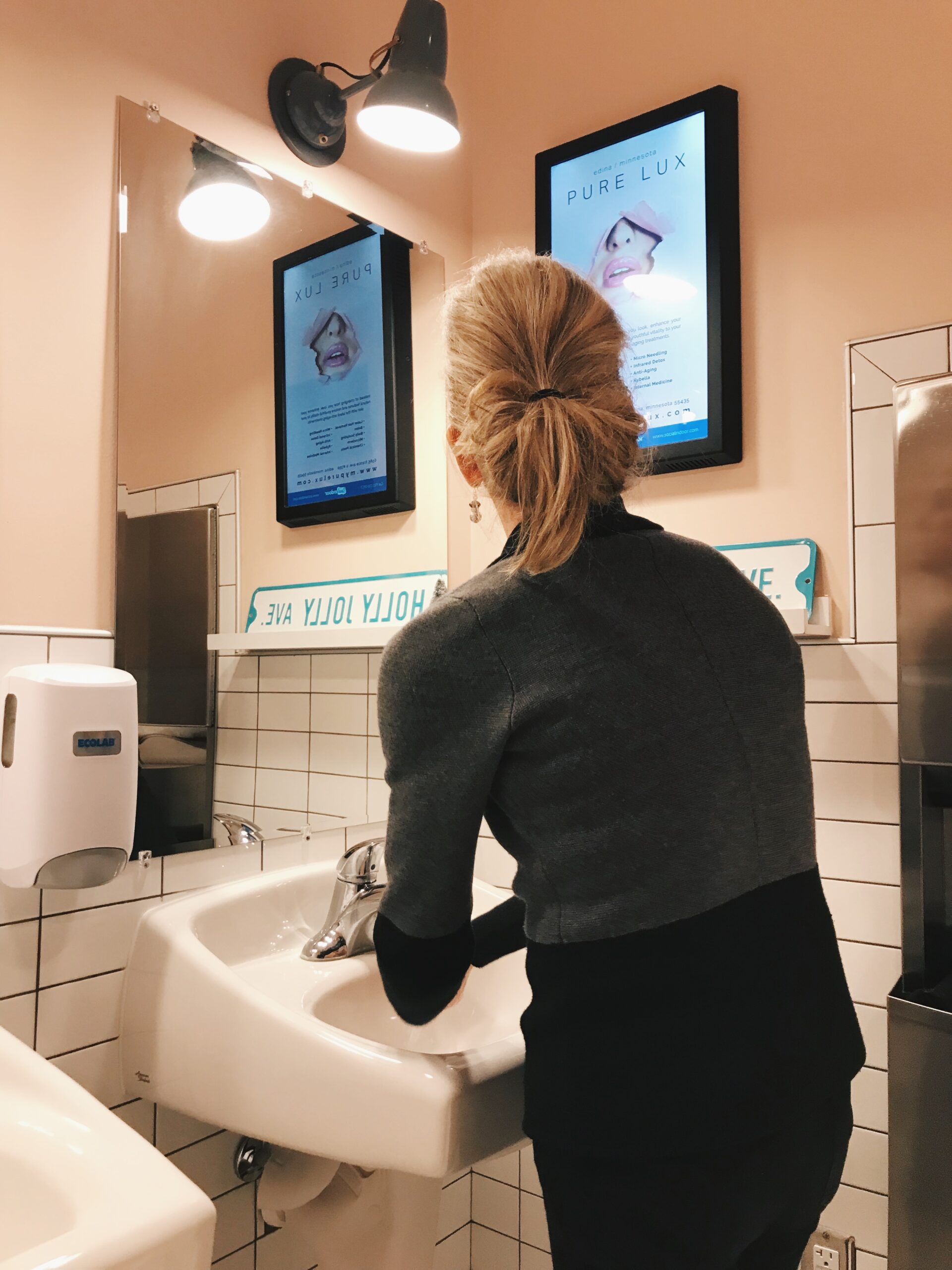 Woman looking at Social Indoor digital indoor advertisement in restroom